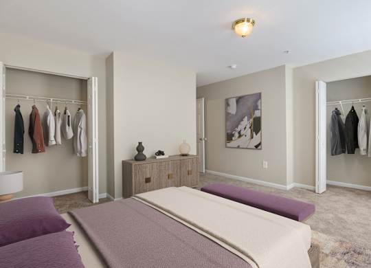 A bedroom with a large bed and a closet with clothes hanging.